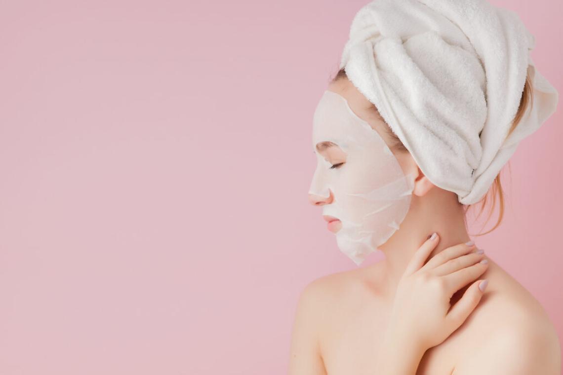 Beautiful young woman is applying a cosmetic tissue mask on a face on a pink background. Healthcare and beauty treatment and technology concept