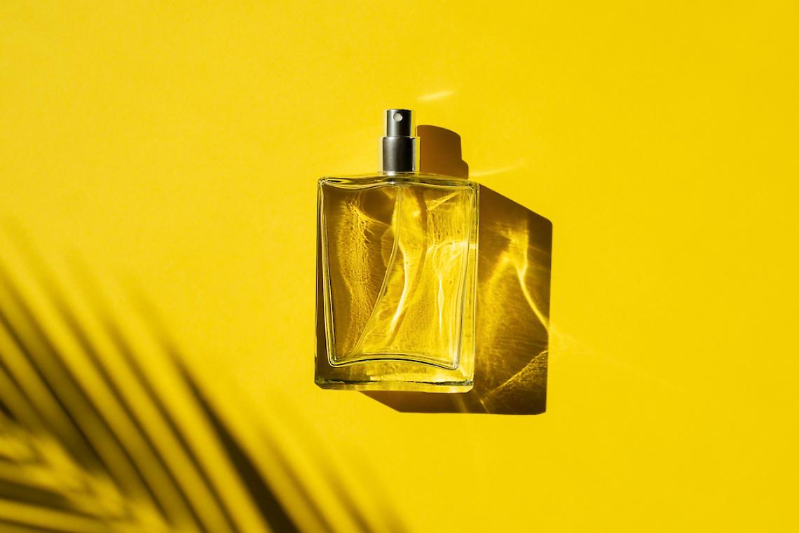 Transparent bottle of perfume with label on a yellow background. Fragrance presentation with daylight.