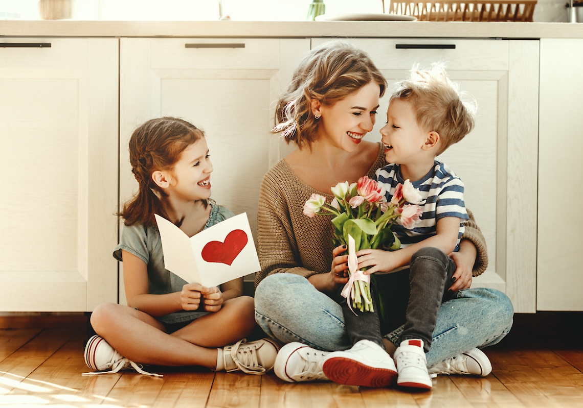Little children congratulating mother in kitchen