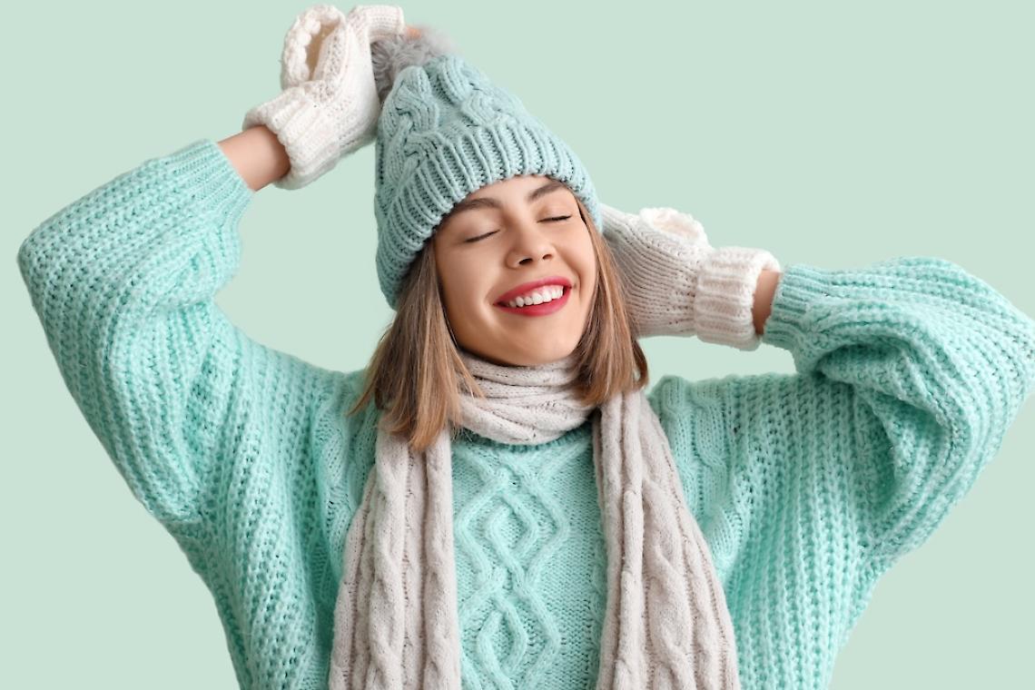 Frozen young woman in winter clothes on green background