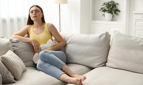 Woman using hot water bottle to relieve menstrual pain on sofa at home