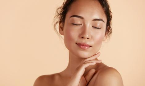 Beauty face Woman with natural makeup and healthy skin portrait Beautiful asian girl model touching fresh glowing hydrated facial skin on beige background closeup Skin care concept