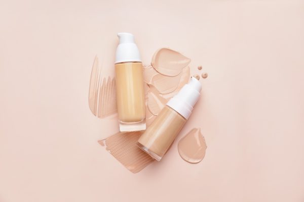 Bottles of makeup foundation and samples on color background