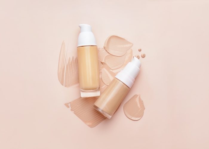 Bottles of makeup foundation and samples on color background