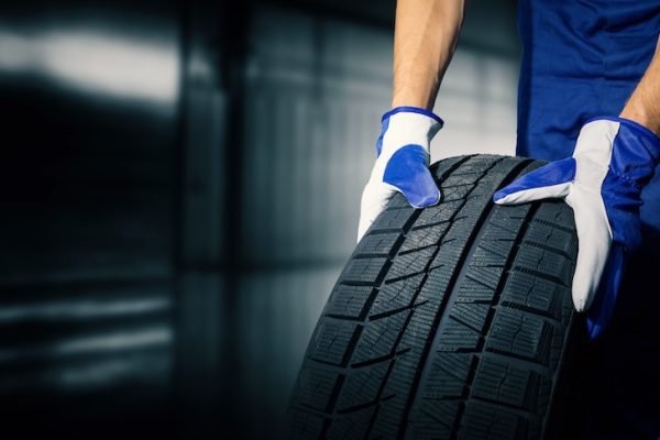 car tire shop and service mechanic holding new tyre on garage background copy space