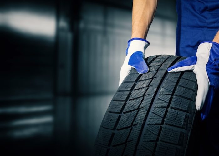 car tire shop and service mechanic holding new tyre on garage background copy space