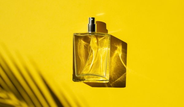 Transparent bottle of perfume with label on a yellow background. Fragrance presentation with daylight. Trending concept in natural materials with beautiful shadow. Women's essence.