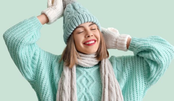 Frozen young woman in winter clothes on green background