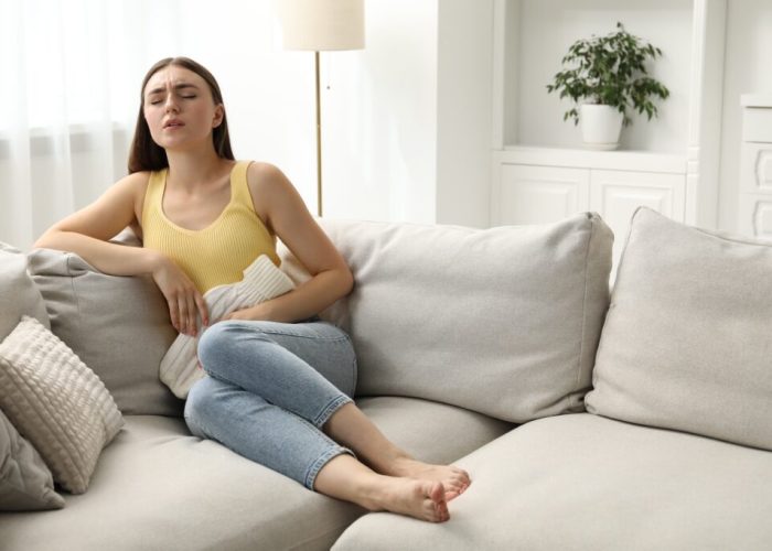 Woman using hot water bottle to relieve menstrual pain on sofa at home