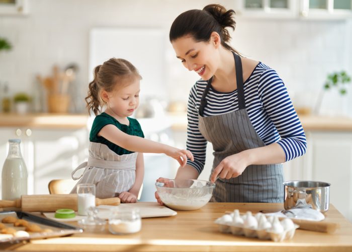 Happy loving family are preparing bakery together. Mother and child daughter girl are cooking cookies and having fun in the kitchen. Homemade food and little helper.