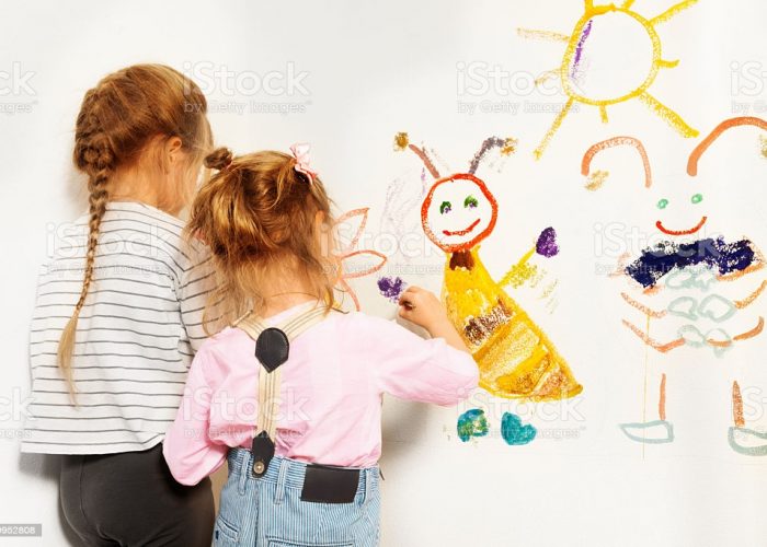 Two little painters, preschool girls drawing funny picture at the wall, isolated on white