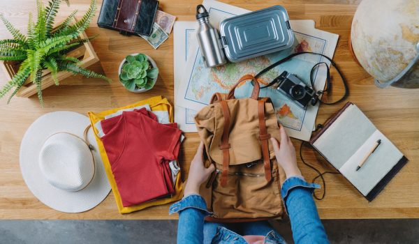 Top view of young woman packing backpack for vacation trip holiday, desktop travel concept.