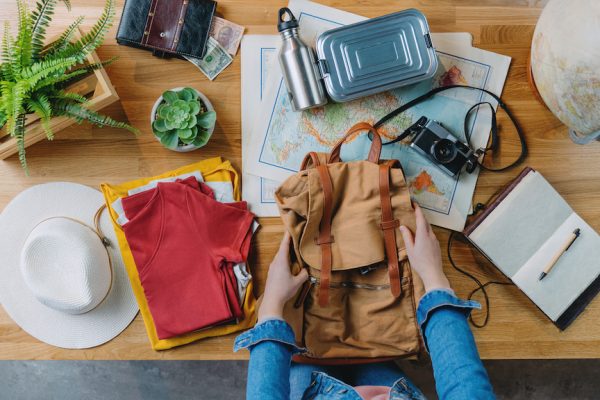 Top view of young woman packing backpack for vacation trip holiday, desktop travel concept.